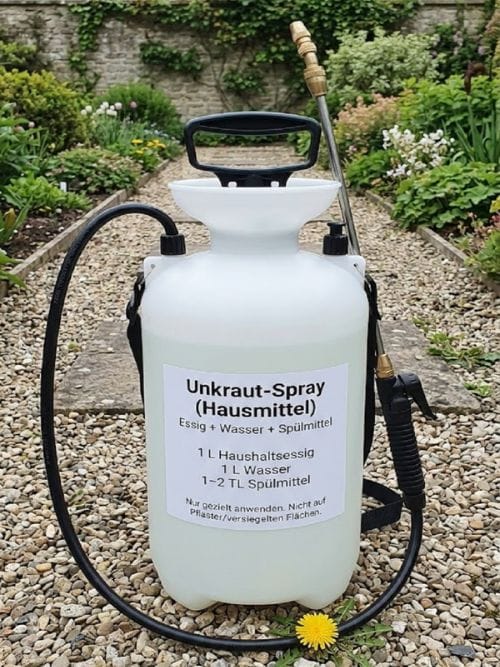 Weiße Pumpsprühflasche im Garten mit Aufschrift Unkraut-Spray Hausmittel Essig Wasser Spülmittel und Hinweis nur gezielt anwenden